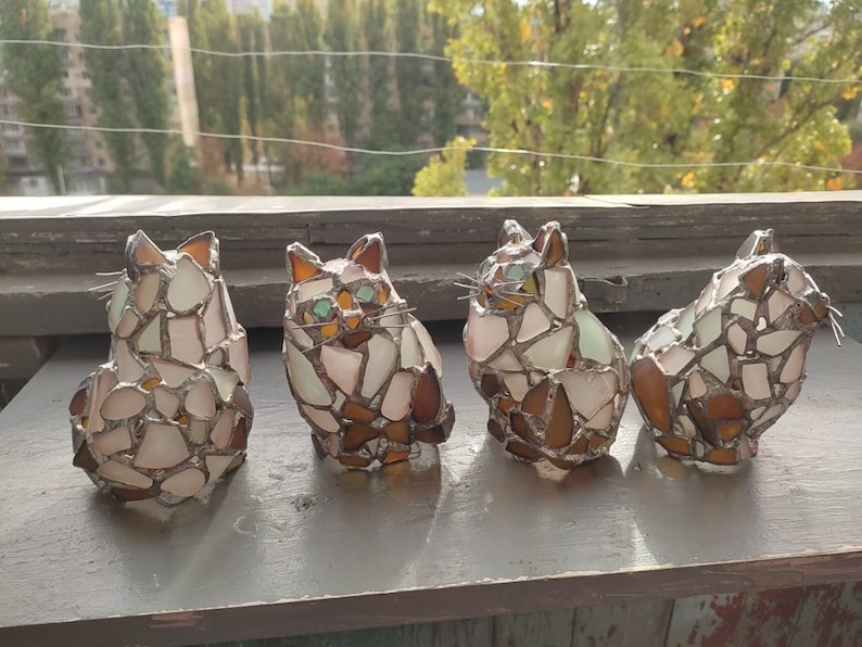 May include: Four mosaic glass cat figurines in white, brown, and green tones. The cats are arranged in a row, facing the same direction.