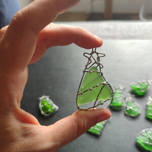 May include: A collection of green glass Christmas tree ornaments wrapped in silver wire. The ornaments are handmade and feature a variety of shapes and sizes.