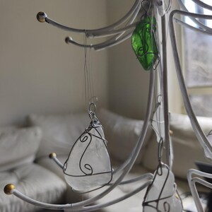 May include: A white metal tree-shaped display stand with ornaments. The ornaments are made of clear and green glass, wrapped in wire. The stand has gold-colored tips on the branches. The ornaments are teardrop-shaped.