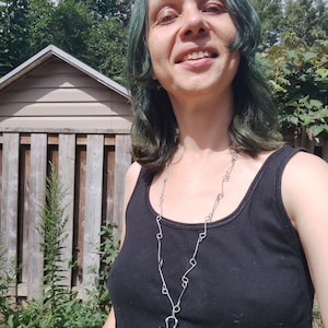 K&ouml;nnte beinhalten: Eine Person mit gr&uuml;nen Haaren tr&auml;gt ein schwarzes Tanktop und eine silberne Kettenkette mit einem t&uuml;rkisfarbenen Schildkr&ouml;tenanh&auml;nger.