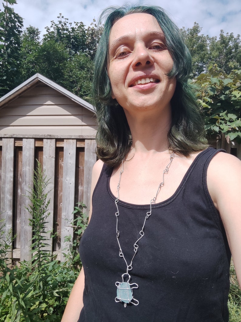 K&ouml;nnte beinhalten: Eine Person mit gr&uuml;nen Haaren tr&auml;gt ein schwarzes Tanktop und eine silberne Kettenkette mit einem t&uuml;rkisfarbenen Schildkr&ouml;tenanh&auml;nger.