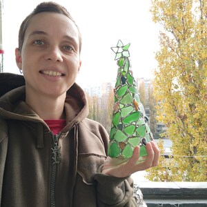 Pode incluir: Uma &aacute;rvore de Natal artesanal feita de vidro do mar verde e transparente. A &aacute;rvore tem formato de cone com uma estrela no topo. O vidro do mar &eacute; mantido unido por metal prateado. A &aacute;rvore tem aproximadamente 20 cm de altura.