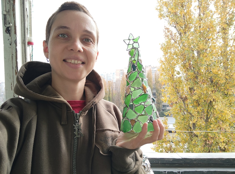 Pode incluir: Uma &aacute;rvore de Natal artesanal feita de vidro do mar verde e transparente. A &aacute;rvore tem formato de cone com uma estrela no topo. O vidro do mar &eacute; mantido unido por metal prateado. A &aacute;rvore tem aproximadamente 20 cm de altura.