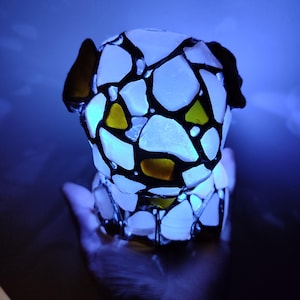 May include: A white glass sculpture of a dog, with black lines and yellow accents, illuminated from within.