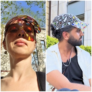 May include: Two people wearing colorful, patterned baseball caps. The caps have a stained-glass effect, with vibrant colors and geometric designs. The caps are worn outdoors in natural light, creating a play of light and shadow.