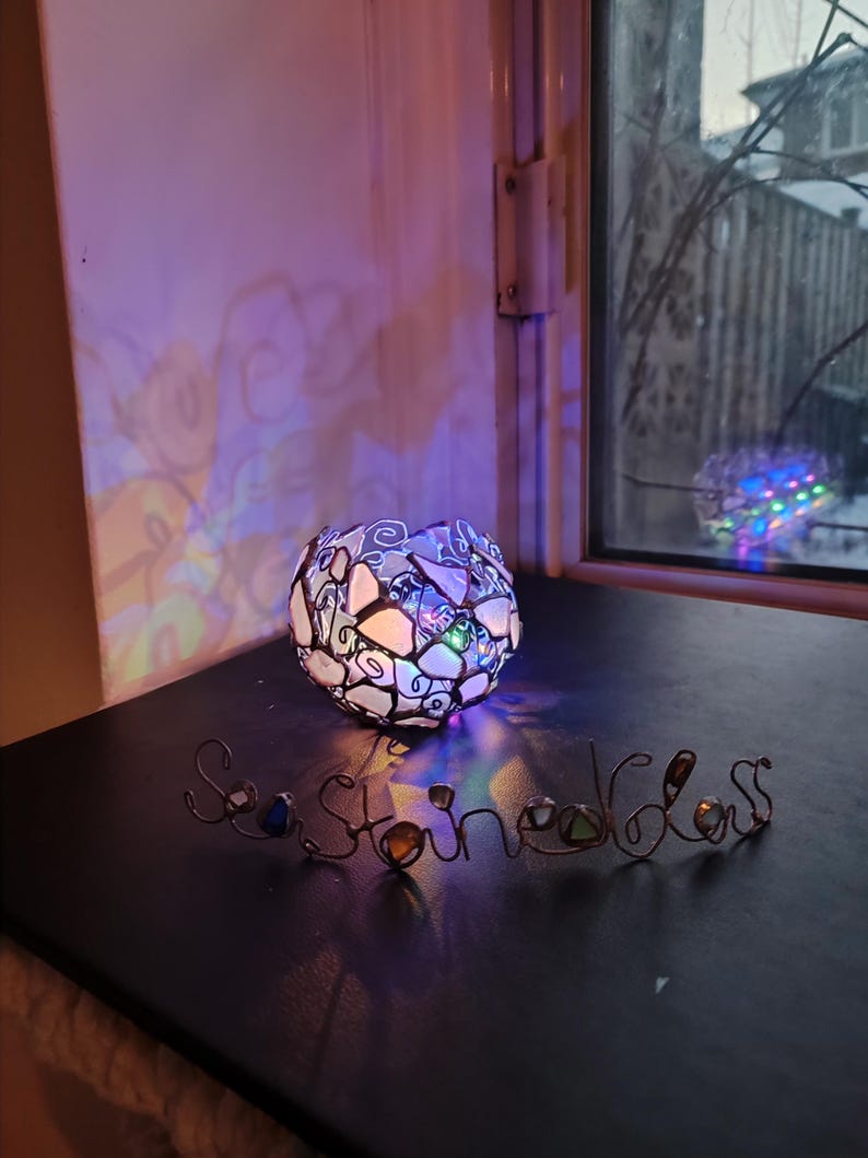 May include: A stained glass lamp with a colorful light cast on a black surface. The word "Seastone" is spelled out in wire with colorful stones.