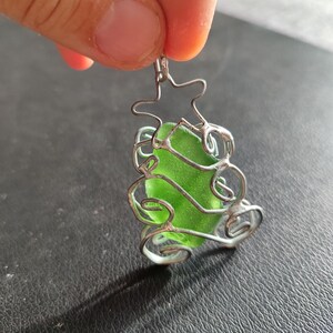 May include: A green glass sea glass charm encased in a silver wire tree design.