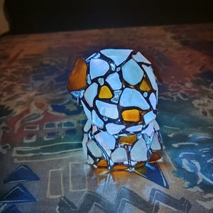 May include: A stained glass lamp shaped like a dog. The lamp is made of white and yellow glass pieces and has a brown outline. The lamp is lit and casting a warm glow.