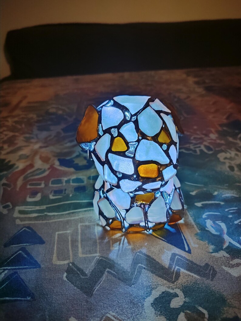 May include: A stained glass lamp shaped like a dog. The lamp is made of white and yellow glass pieces and has a brown outline. The lamp is lit and casting a warm glow.