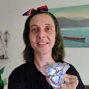 May include: A person is holding a small, clear glass sculpture that resembles a cup. The sculpture is made of many small pieces of glass that are held together with silver wire. The sculpture is lit from within, creating a warm glow.