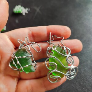 May include: Two green glass pieces are encased in silver wire, creating a unique and delicate design. The wire is twisted and shaped to resemble a tree or a plant.