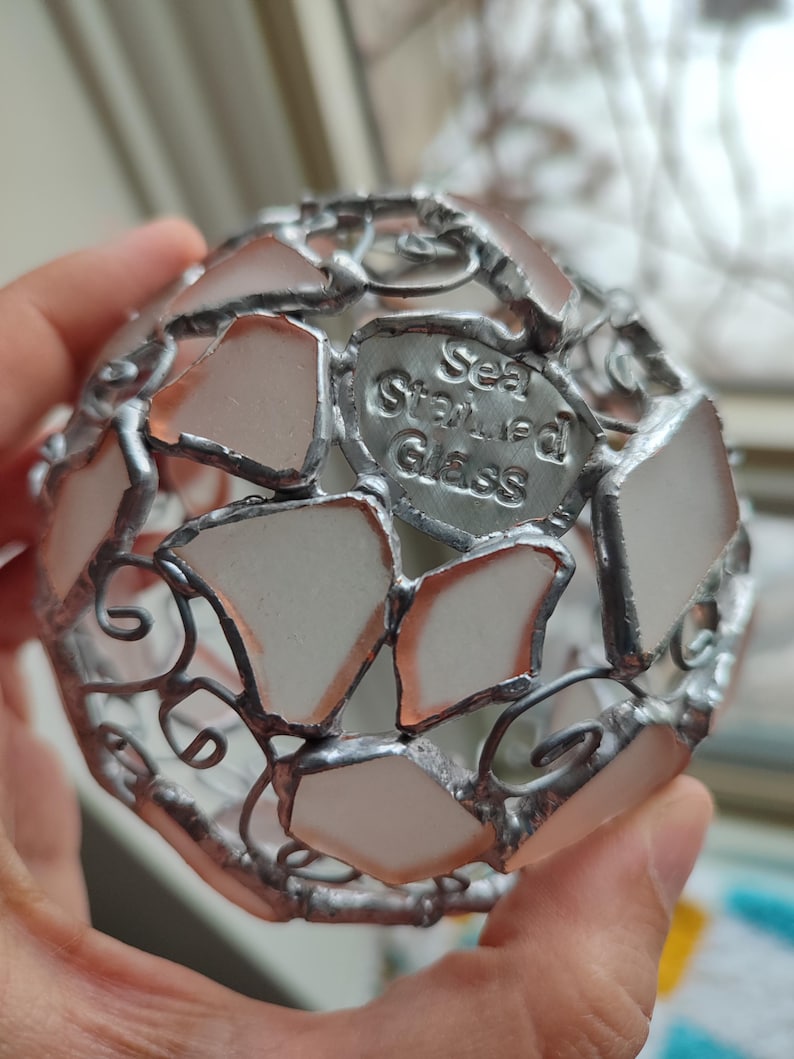 May include: A silver metal sphere made of sea glass pieces, with a label that reads "Sea Stained Glass".