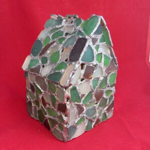 May include: A small house-shaped box made of sea glass and silver. The box is decorated with pieces of sea glass in shades of green, brown, and white.