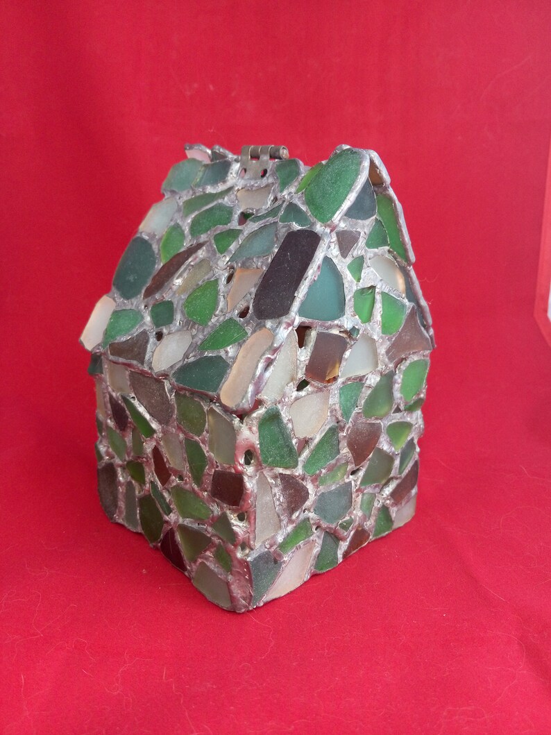 May include: A small house-shaped box made of sea glass and silver. The box is decorated with pieces of sea glass in shades of green, brown, and white.