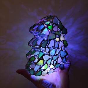 K&ouml;nnte beinhalten: Eine Tiffany-Lampe in Form eines Baumes, mit gr&uuml;nen, blauen und wei&szlig;en Glasscheiben. Die Lampe ist mit bunten Lichtern beleuchtet, was einen wundersch&ouml;nen und fantasievollen Effekt erzeugt.
