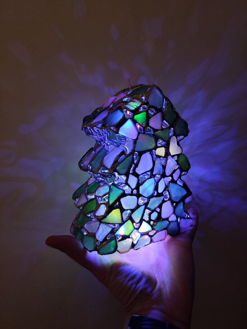 K&ouml;nnte beinhalten: Eine Tiffany-Lampe in Form eines Baumes, mit gr&uuml;nen, blauen und wei&szlig;en Glasscheiben. Die Lampe ist mit bunten Lichtern beleuchtet, was einen wundersch&ouml;nen und fantasievollen Effekt erzeugt.