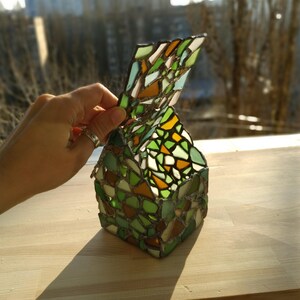 May include: A small, green, yellow and brown stained glass box with a hinged lid. The box is made of small pieces of glass that are arranged in a mosaic pattern.