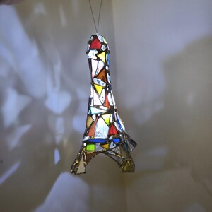 May include: A stained glass Eiffel Tower ornament in a variety of colours. The miniature tower is made from pieces of red, yellow, blue, and white glass. It is suspended by a thin wire.