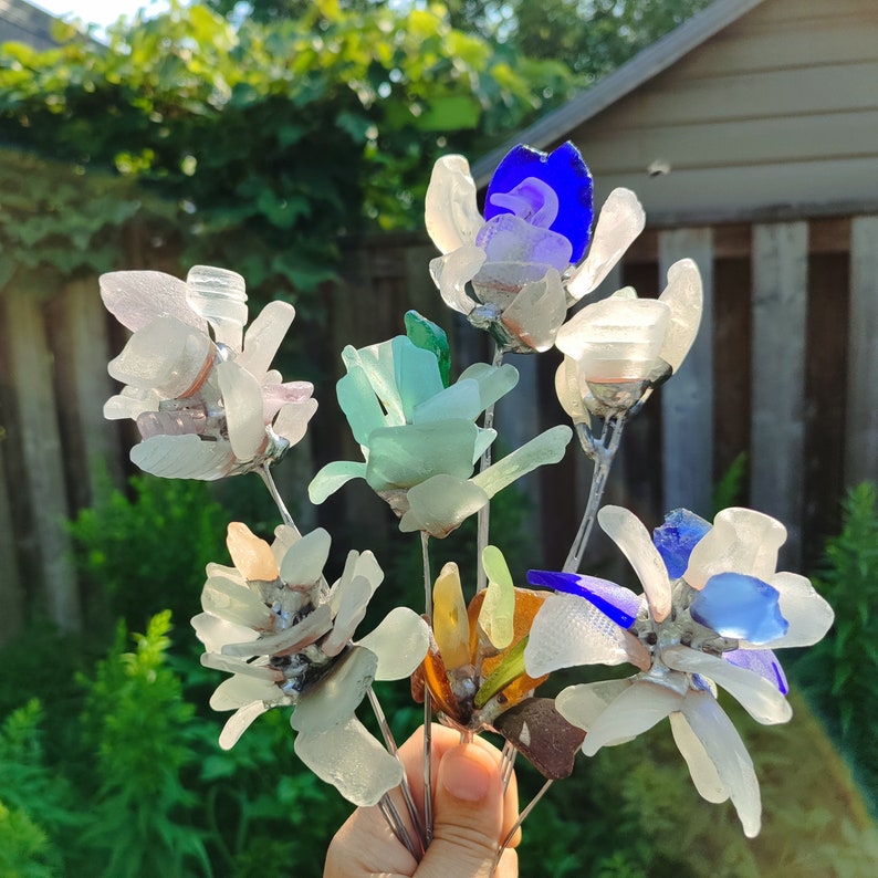 Op de afbeelding: Een boeket van kleurrijke glazen bloemen met blauwe, groene en witte accenten. De bloemen zijn gerangschikt op draadstengels en zijn perfect voor een uniek decor voor thuis.