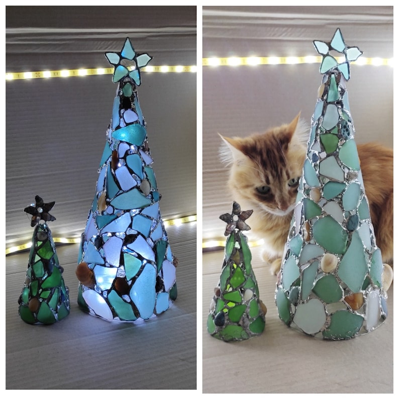 Pode incluir: Duas &aacute;rvores de Natal decorativas feitas de vidro do mar. A &aacute;rvore maior &eacute; verde-azulado e azul, com uma estrela no topo. A &aacute;rvore menor &eacute; verde. Ambas as &aacute;rvores t&ecirc;m formato de cone e s&atilde;o iluminadas com luzes internas.