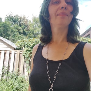 K&ouml;nnte beinhalten: Eine Frau mit blaugr&uuml;nem Haar tr&auml;gt ein schwarzes Tanktop und eine silberne Kettenkette mit einem gr&uuml;nen Steint&uuml;r-Anh&auml;nger.