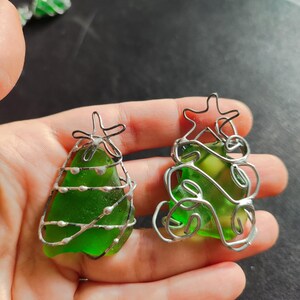 May include: Two green glass Christmas tree ornaments wrapped in silver wire. The ornaments are different shapes and sizes.