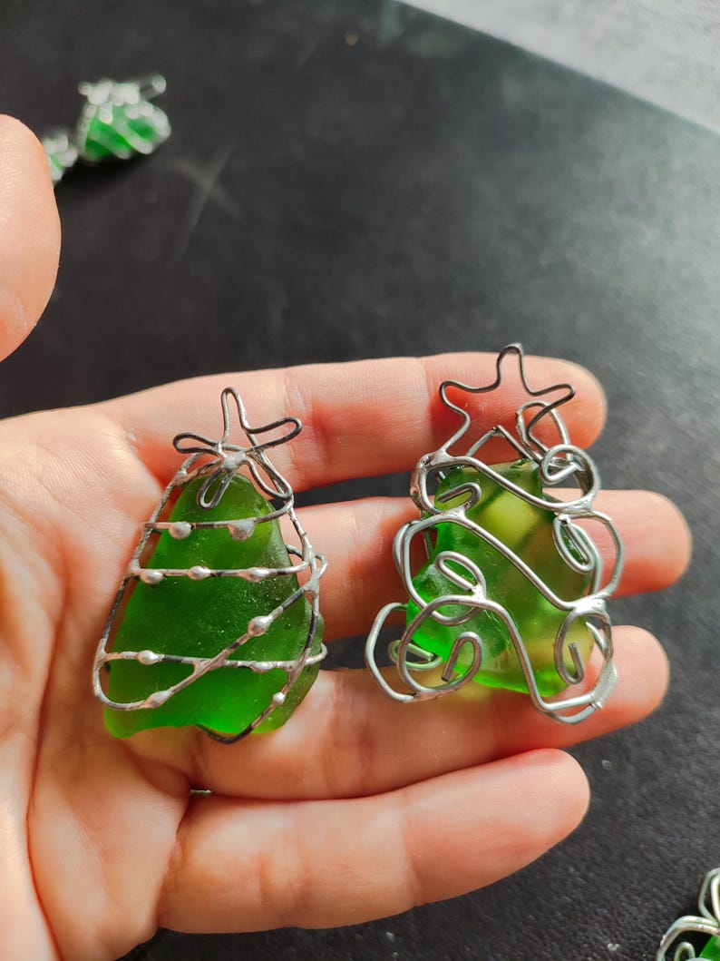 May include: Two green glass Christmas tree ornaments wrapped in silver wire. The ornaments are different shapes and sizes.