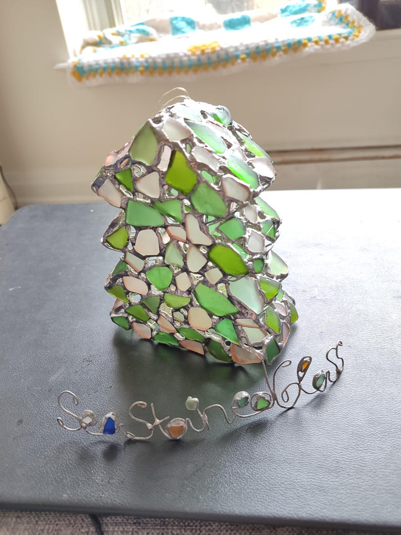 K&ouml;nnte beinhalten: Ein gr&uuml;ner und wei&szlig;er Glasmosaik-Anh&auml;nger in Form eines Baumes mit den Worten "Sea Glass" in Draht darunter.