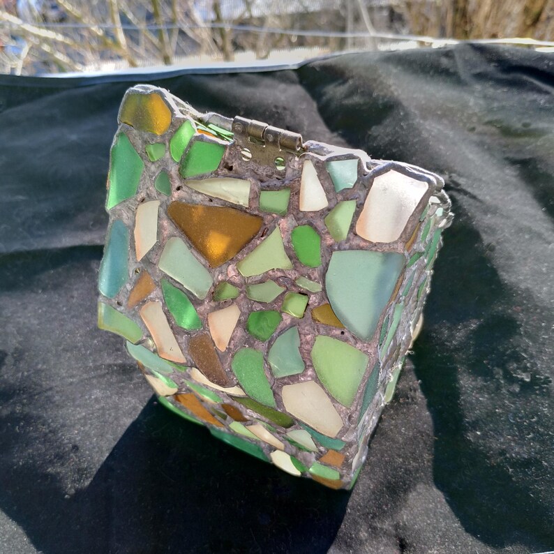 May include: A small box made of mosaic tiles. The tiles are various shades of green, brown, and white. The box has a metal hinge.