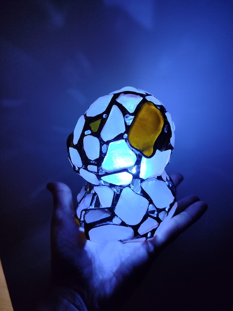 May include: A white and black mosaic lamp with a yellow glass accent. The lamp is lit and glowing blue.