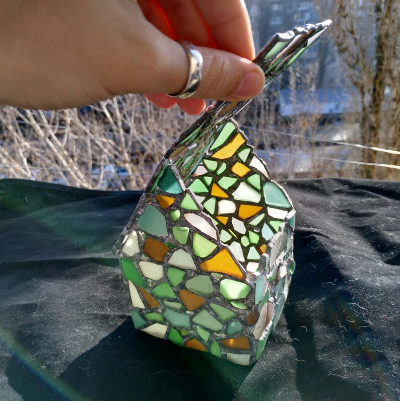 May include: A small, green, yellow and white stained glass house-shaped candle holder. The holder is made of small pieces of glass that are fused together.