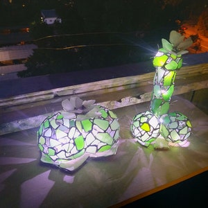 May include: Two green glass mosaic sculptures of a cactus, one upright and one laying down, illuminated from within.