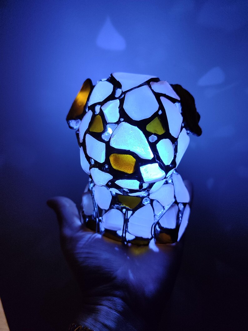 May include: A white and yellow stained glass dog figurine with black accents. The figurine is illuminated from within, casting a blue glow.