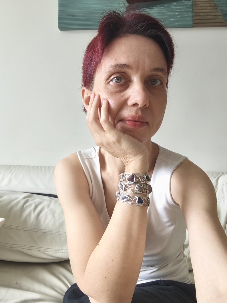 May include: Three silver bracelets with gemstone accents. The bracelets are stacked on top of each other. The gemstones are purple and blue. The bracelets have a wire design.