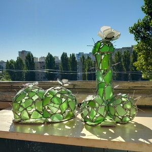 May include: A green glass sculpture of a cactus with a white flower on top. The sculpture is made of many small pieces of glass that are joined together.