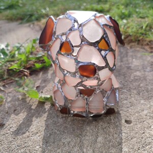 May include: A small, white, glass sculpture of a dog made with stained glass. The dog has brown eyes and is sitting on a concrete surface.