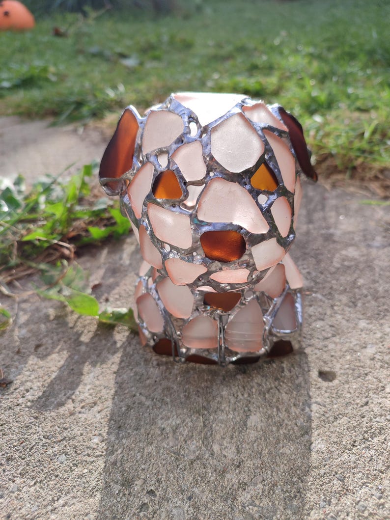 May include: A small, white, glass sculpture of a dog made with stained glass. The dog has brown eyes and is sitting on a concrete surface.