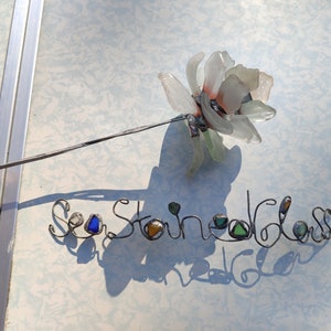 Op de afbeelding: Een witte zeeglasbloem met een draadsteel en de woorden "Sea Stained Glass" geschreven in draad met zeeglasaccenten.