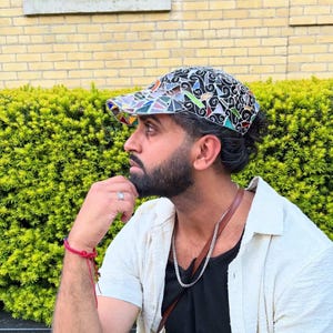 May include: A colorful baseball cap with a mosaic-like design featuring various shapes and colors. The cap has a black background with a mix of blue, green, yellow, and red accents. The brim is also multi-colored.