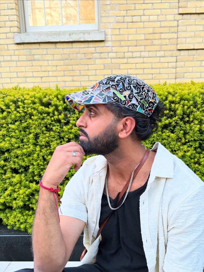 May include: A colorful baseball cap with a mosaic-like design featuring various shapes and colors. The cap has a black background with a mix of blue, green, yellow, and red accents. The brim is also multi-colored.