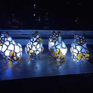 May include: Four stained glass cat figurines with white, yellow, and black glass pieces. The cats are illuminated from within, casting a warm glow.