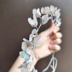 May include: A delicate floral headpiece featuring pale pink, peach, and blue-green gemstone petals. The gemstones are set on a silver-colored wire frame, creating a whimsical and ethereal design. Perfect for weddings or special occasions.