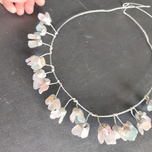 May include: A delicate floral crown with a silver wire base. The crown features clusters of translucent, pastel-colored flower-shaped beads. The beads are in shades of pink, white, and pale green. The crown is designed for a special occasion.
