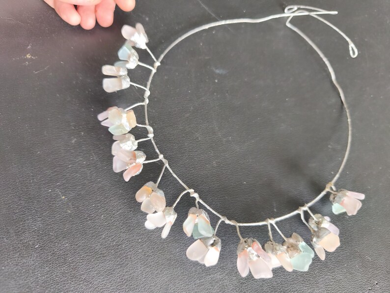 May include: A delicate floral crown with a silver wire base. The crown features clusters of translucent, pastel-colored flower-shaped beads. The beads are in shades of pink, white, and pale green. The crown is designed for a special occasion.