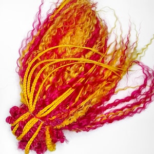 Può includere: Un fascio di extension per capelli dai colori vivaci, giallo, arancione e rosa acceso. Le extension sono acconciate con un mix di ciocche ricce e lisce e sono legate insieme alla base con trecce gialle.
