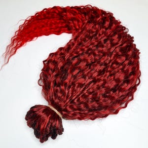May include: A bundle of deep red curly hair extensions, transitioning to a lighter red at the ends. The hair is tied with a natural twine, showcasing a vibrant, textured appearance. Ideal for creating voluminous hairstyles.