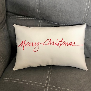 May include: White throw pillow with the words "Merry Christmas" written in red cursive script.