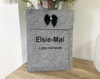 May include: A gray felt book cover with a black bow and a rhinestone. The cover is personalized with the name "Elsie-Mai" and the text "Little red book".