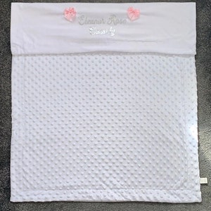 May include: White baby blanket with a white satin border and pink satin bows. The blanket is personalized with the name "Eleanor Rose" and the word "Sweetly" in silver embroidery.