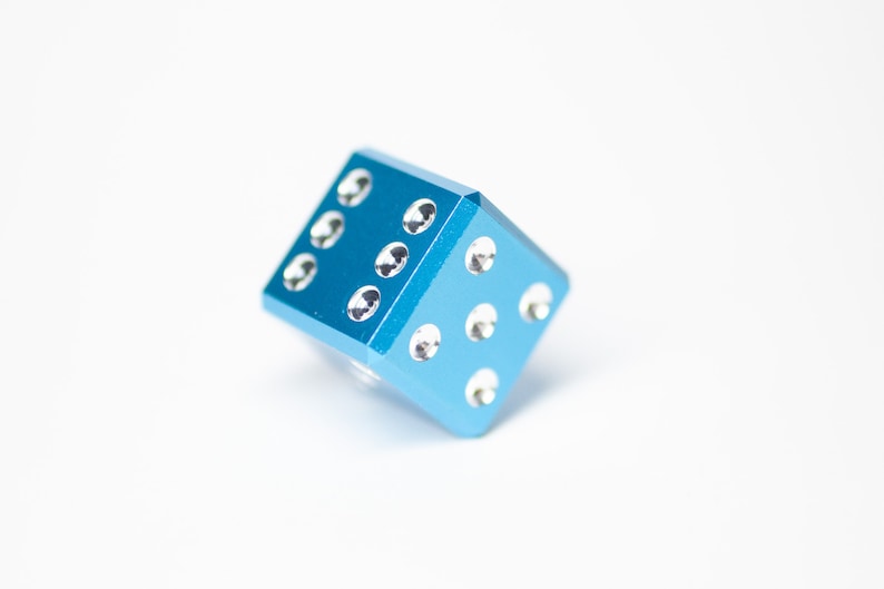 Puede incluir: Un dado de metal azul con puntos blancos. El dado est&aacute; tumbado de lado.